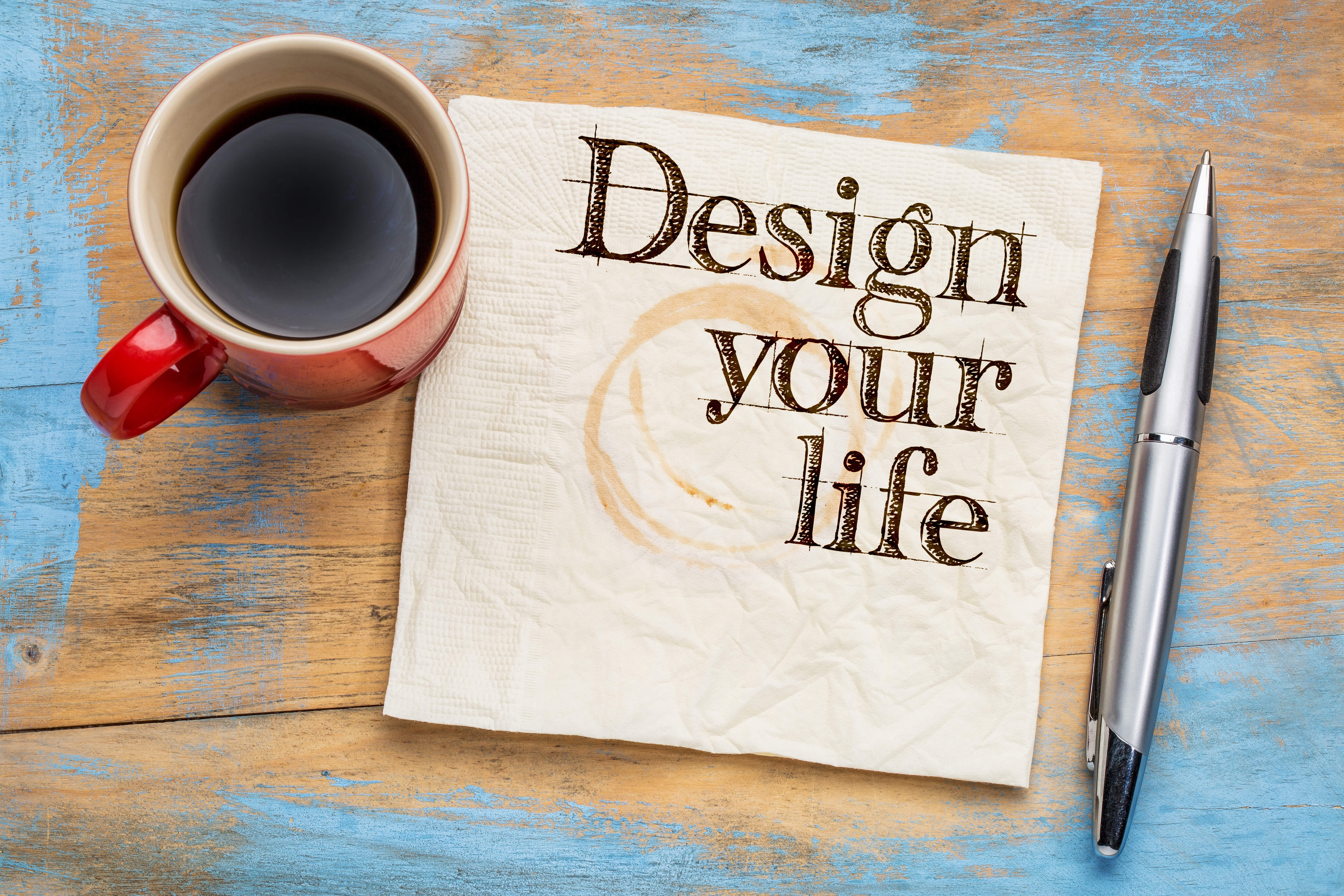 ティーカップにはいったコーヒーとペンと「Design your life」と書かれた紙のイメージ画像